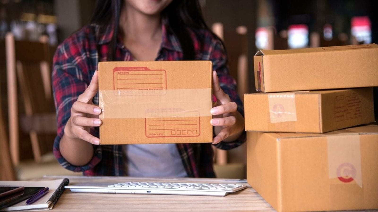 A woman is holding a box of boxes in front of a computer.