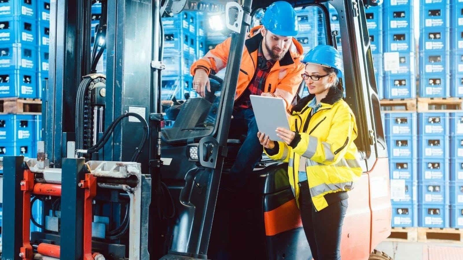 Two people working on a forklift in a warehouse.